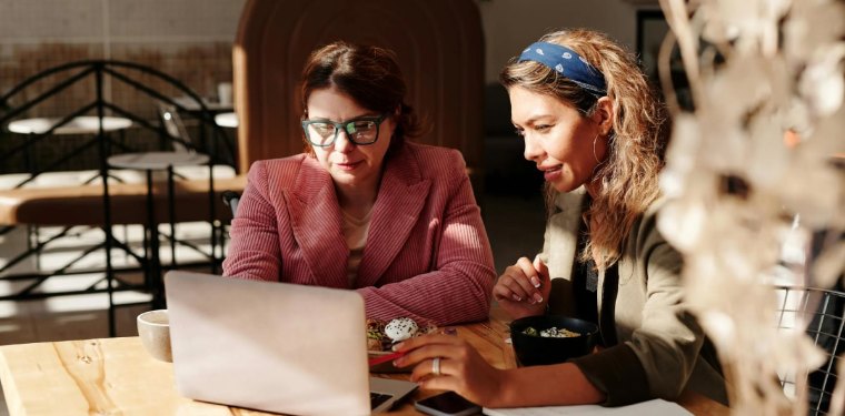 Two women review something on a laptop at a café table